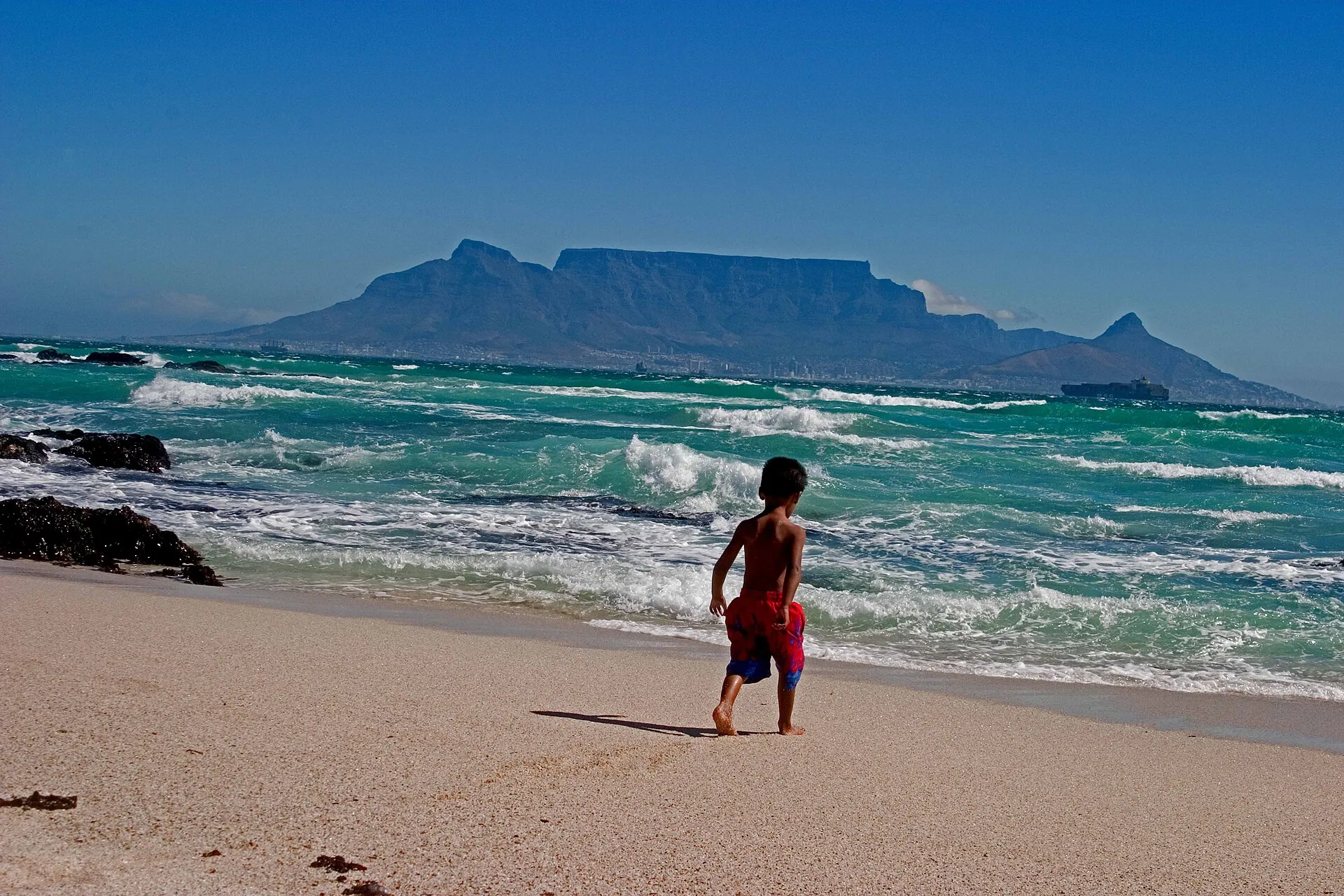 The flat top of Table Mountain seen from a beach across the bay, with the sea in front and Cape Town tucked underneath it.
