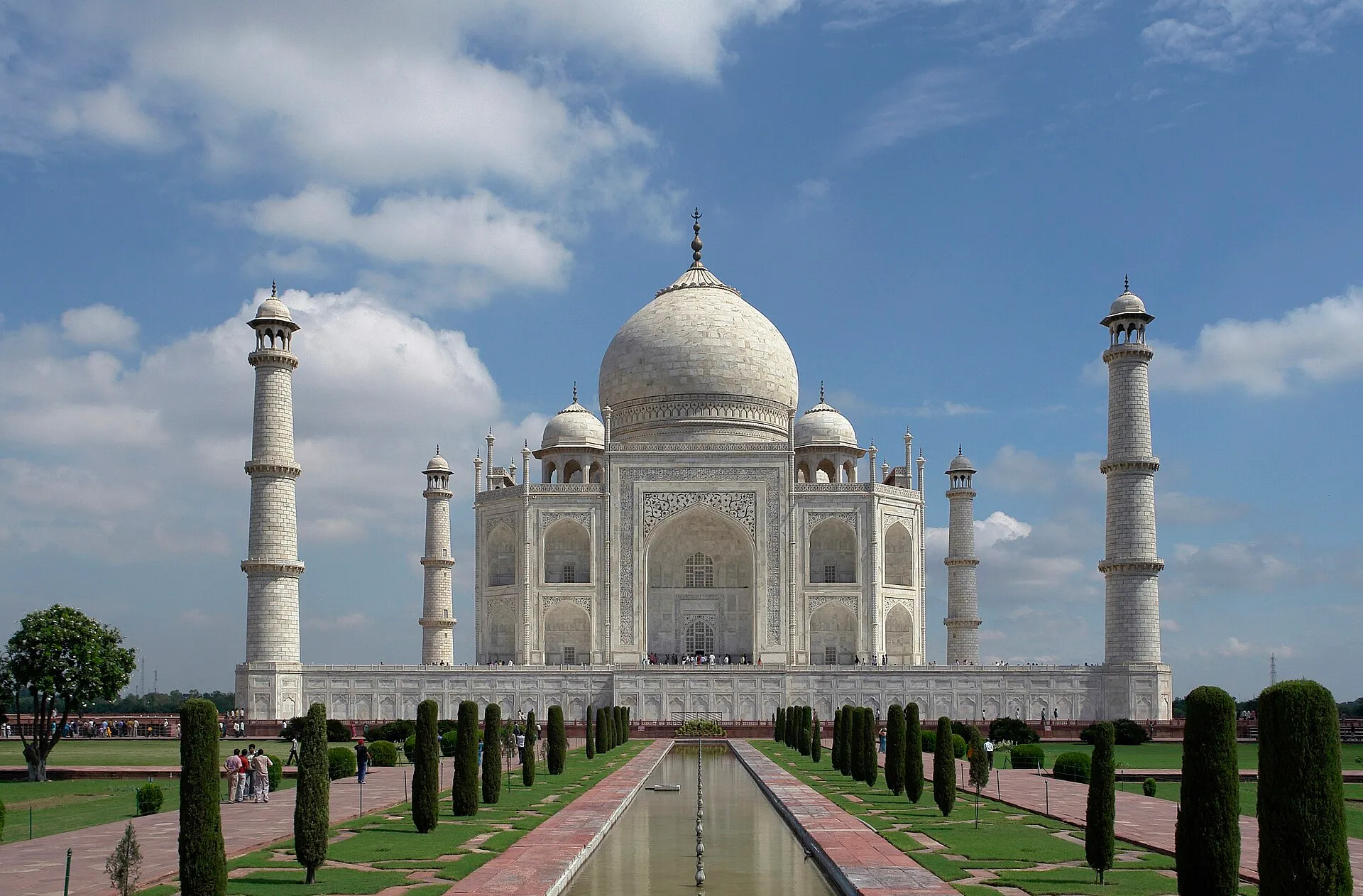 The Taj Mahal in India, a huge white marble building with a big dome and four tall towers, behind a long pool in a green garden.
