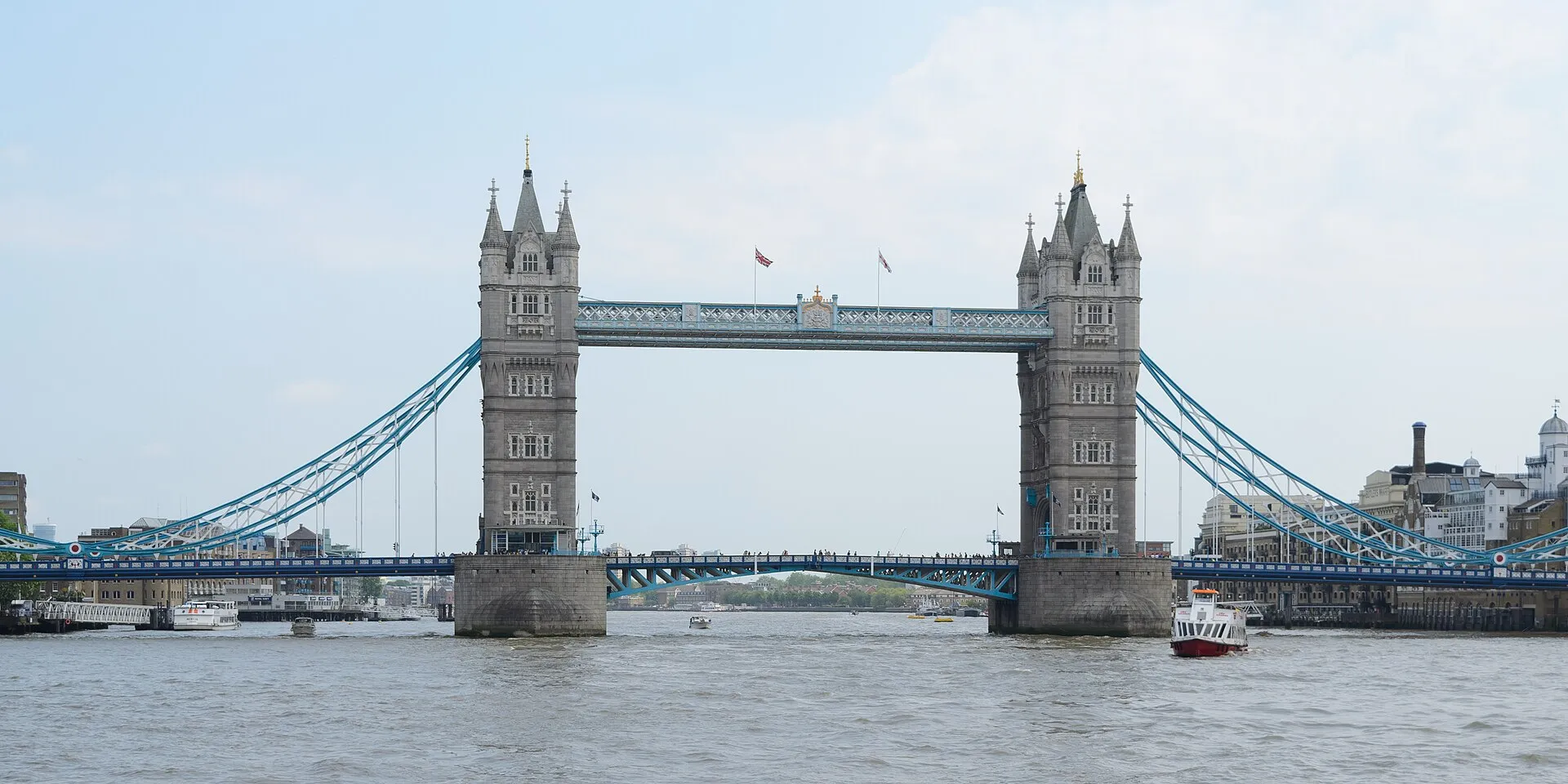 Tower Bridge in London on a bright day, showing its two tall grey towers and light blue bridge arms over the River Thames.